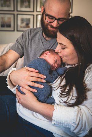 New parents tenderly kiss and cradle their sleeping newborn baby dressed in blue at home.