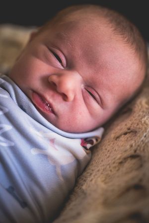 Peaceful newborn baby sleeping soundly, swaddled in white, resting on a soft furry blanket in a cozy setting.