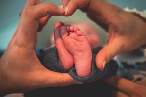 Adult hands forming a heart shape around tiny newborn baby feet wrapped in a blue blanket.