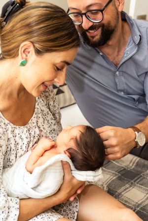 Smiling parents lovingly gazing at their newborn baby wrapped in white blanket during an intimate family moment.