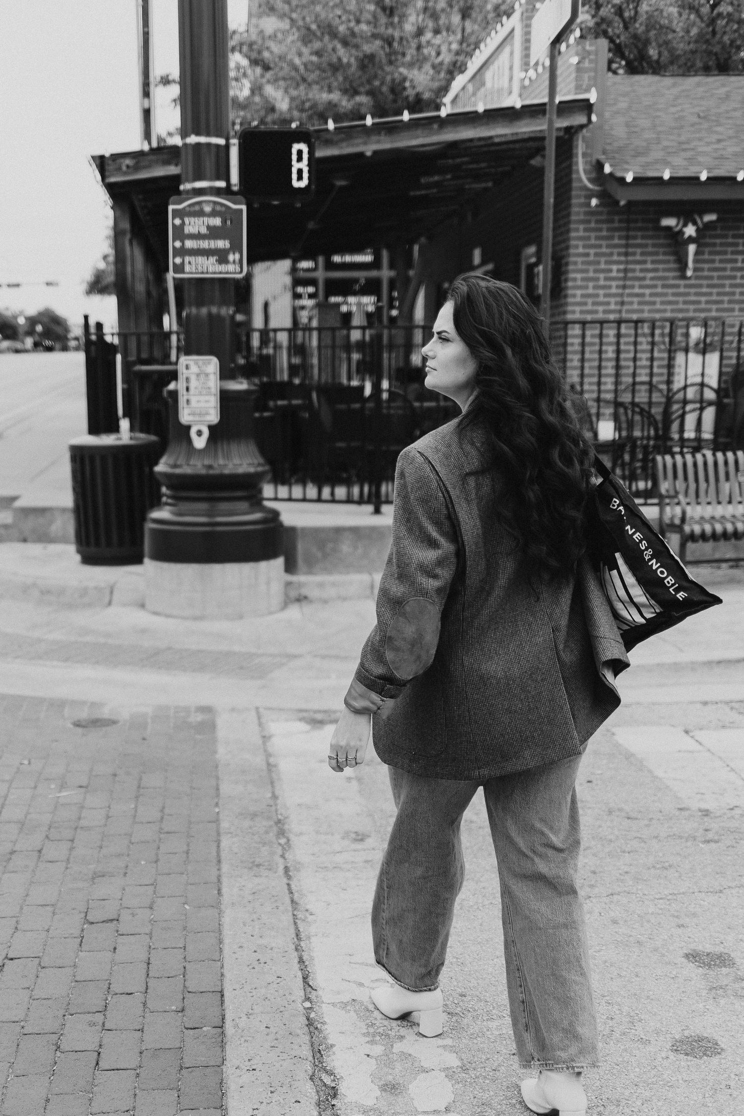 Black and white street photo of someone in an oversized blazer and jeans walking past a brick storefront.