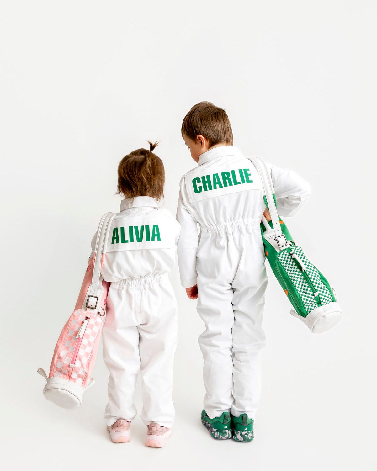 Two children wearing personalized caddy uniforms with green and pink kids golf bags during branding photoshoot.