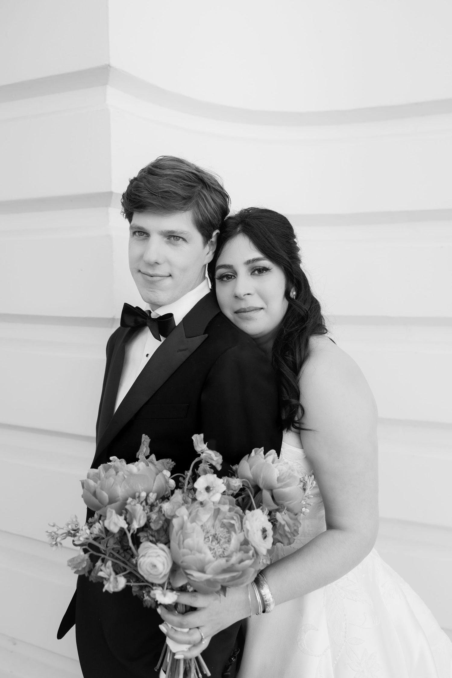 Black and white portrait of a bride and groom posing together, bride holding a floral bouquet, wearing wedding attire.