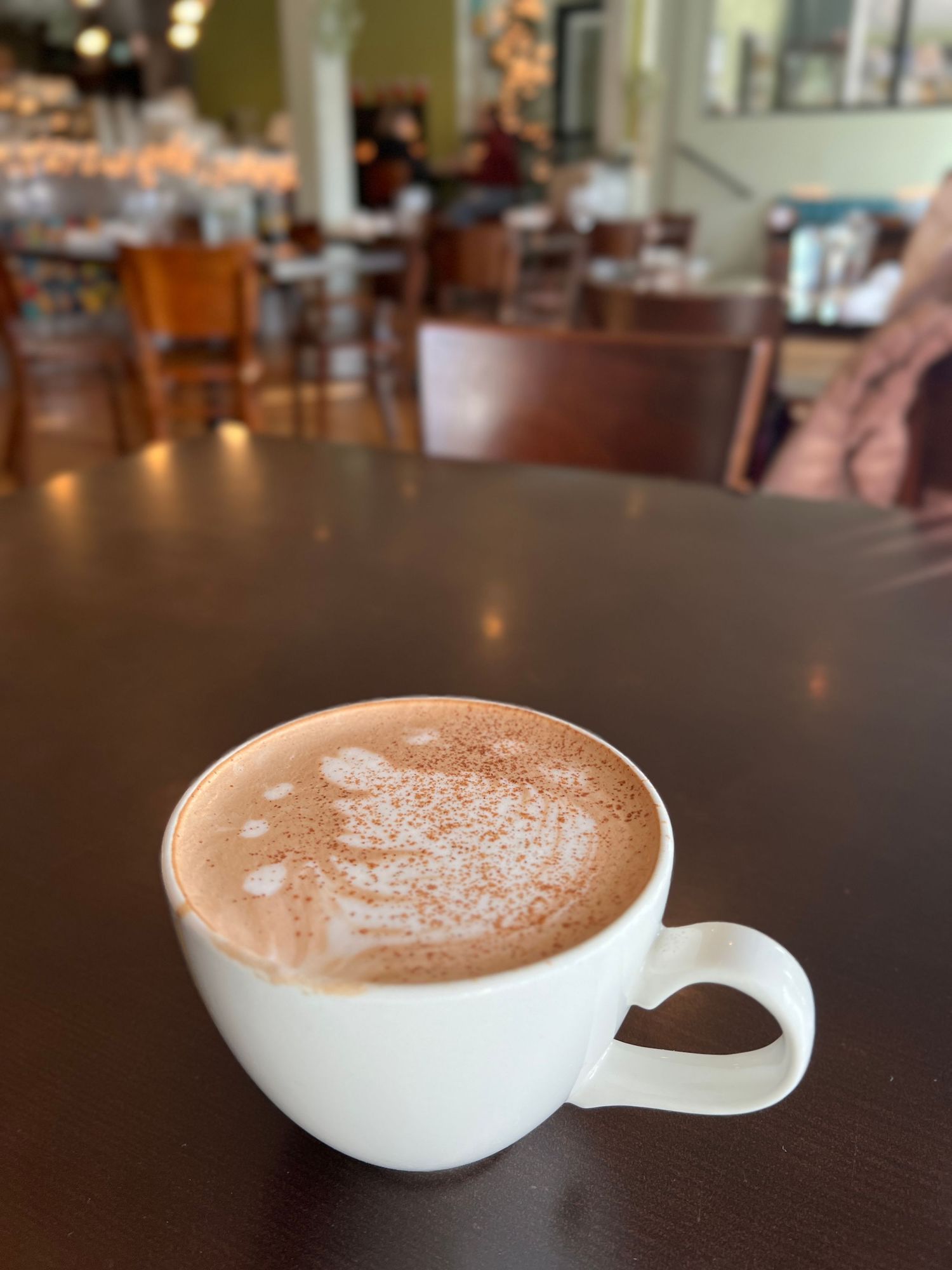 A cup of coffee with a frothy top, sitting on a wooden table in a cafe.