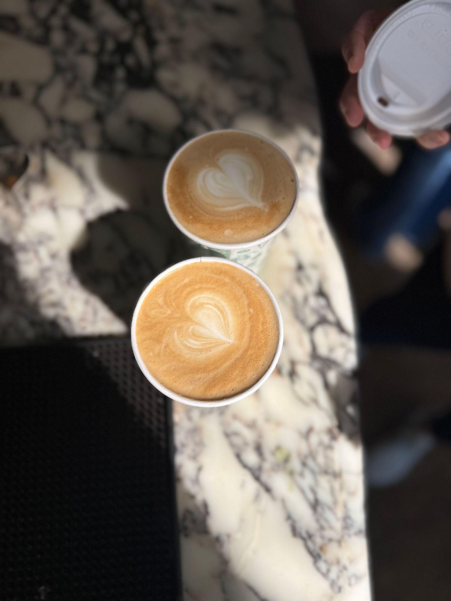 Two cups of coffee with latte art on a marble surface.