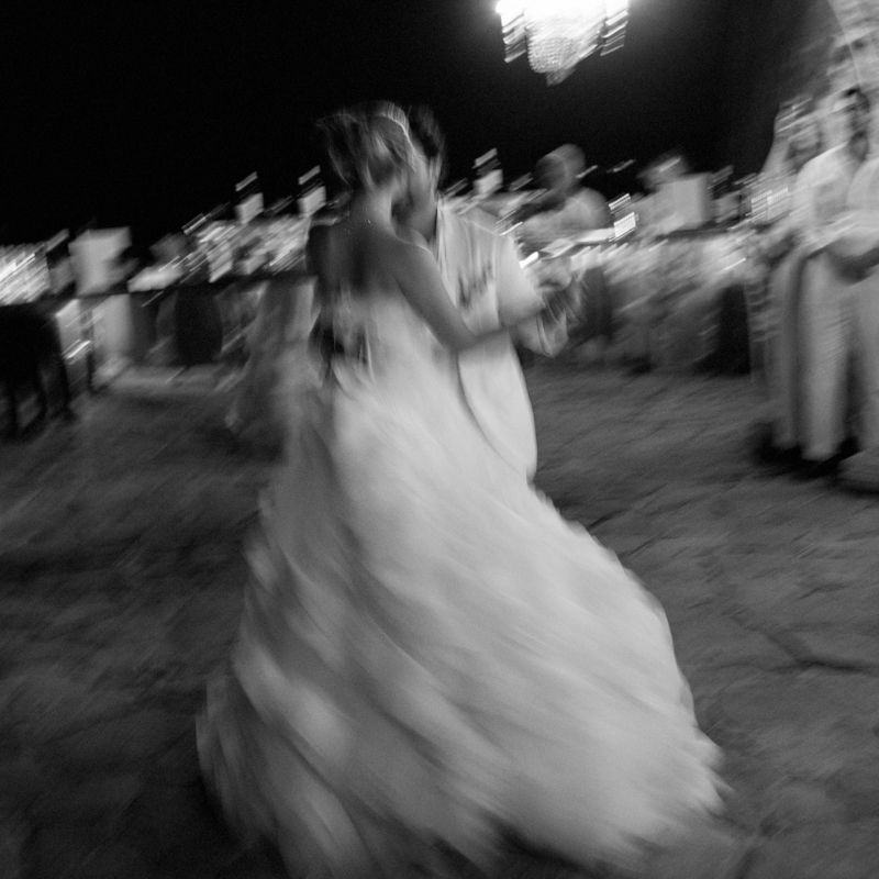 Motion blur captures a bride in a flowing white dress twirling and dancing at a wedding reception.