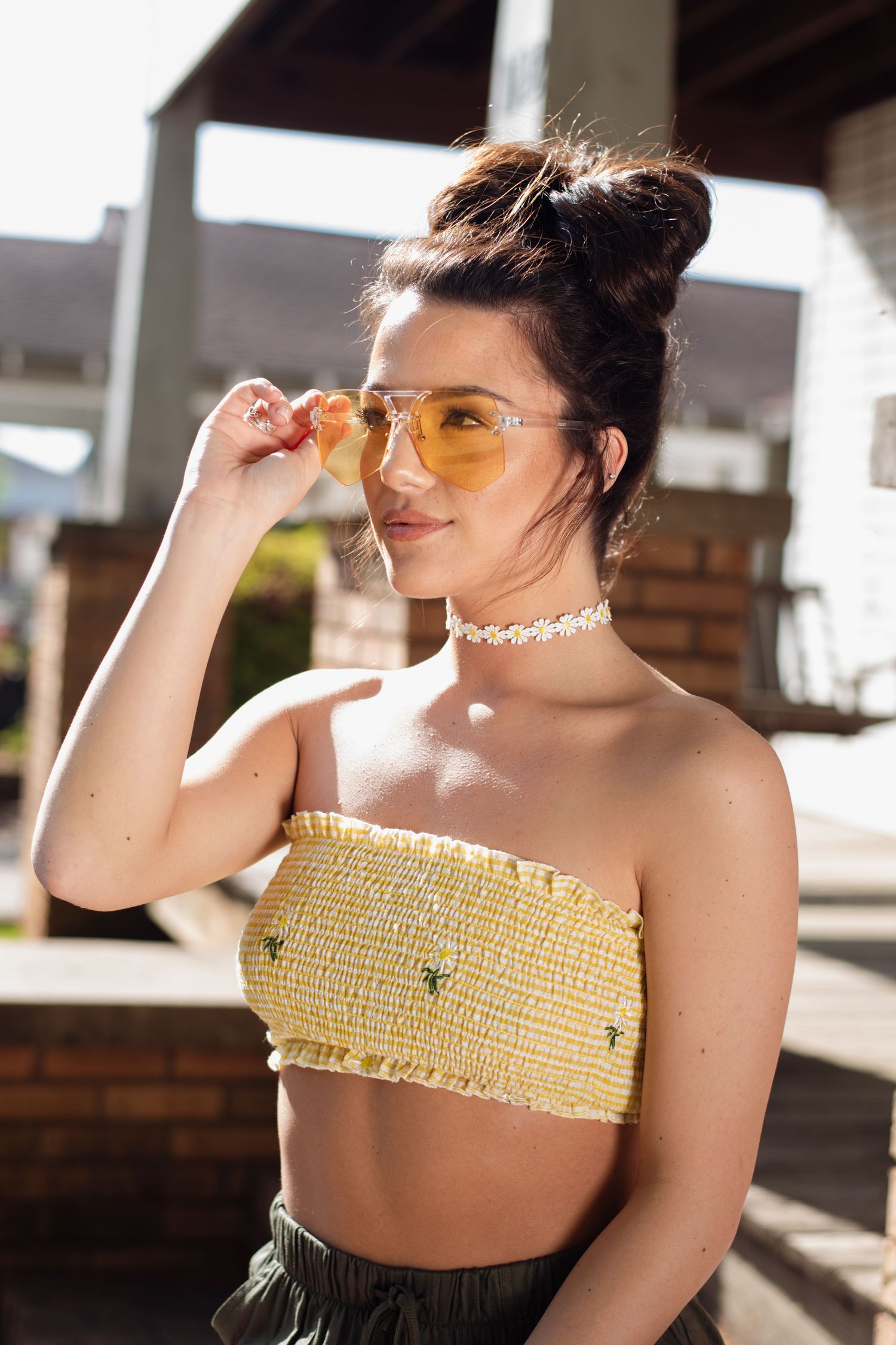 Young woman in yellow strapless crop top and tinted sunglasses posing outdoors in bright sunlight.