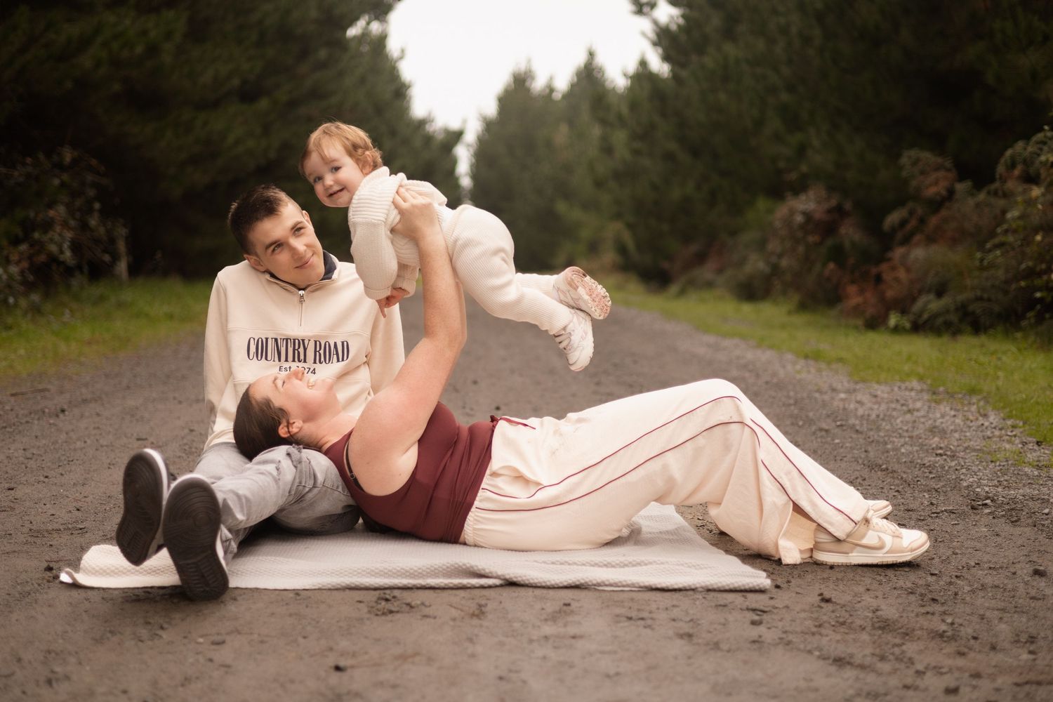 family session at Bottle lake forest, mum lying on dad holding up their toddler, Christchurch
