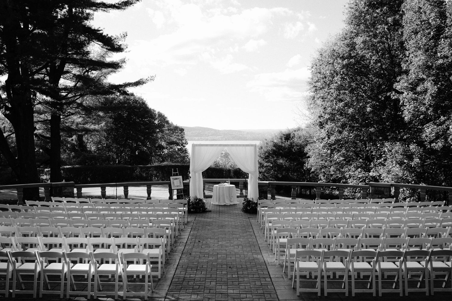 Wedding ceremony setup with white chairs on a lush green lawn facing a historic stone church under cloudy skies.
