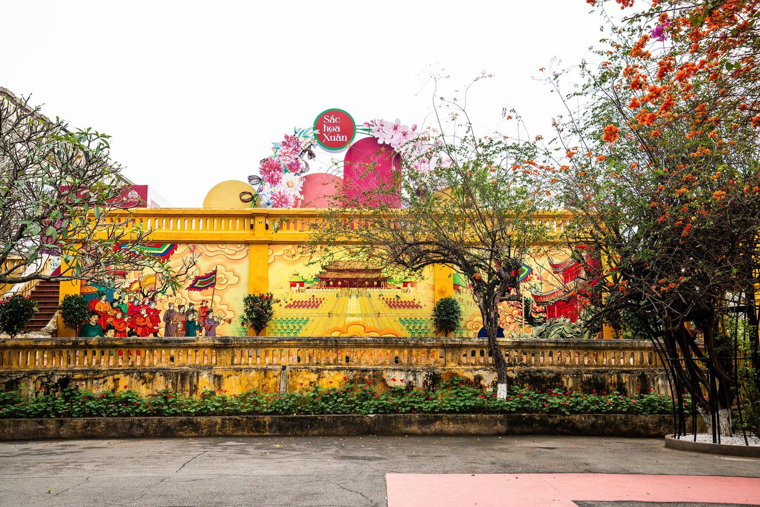 Panoramic view of a Chinese temple complex with red lanterns and cherry blossoms against a golden sunset sky.