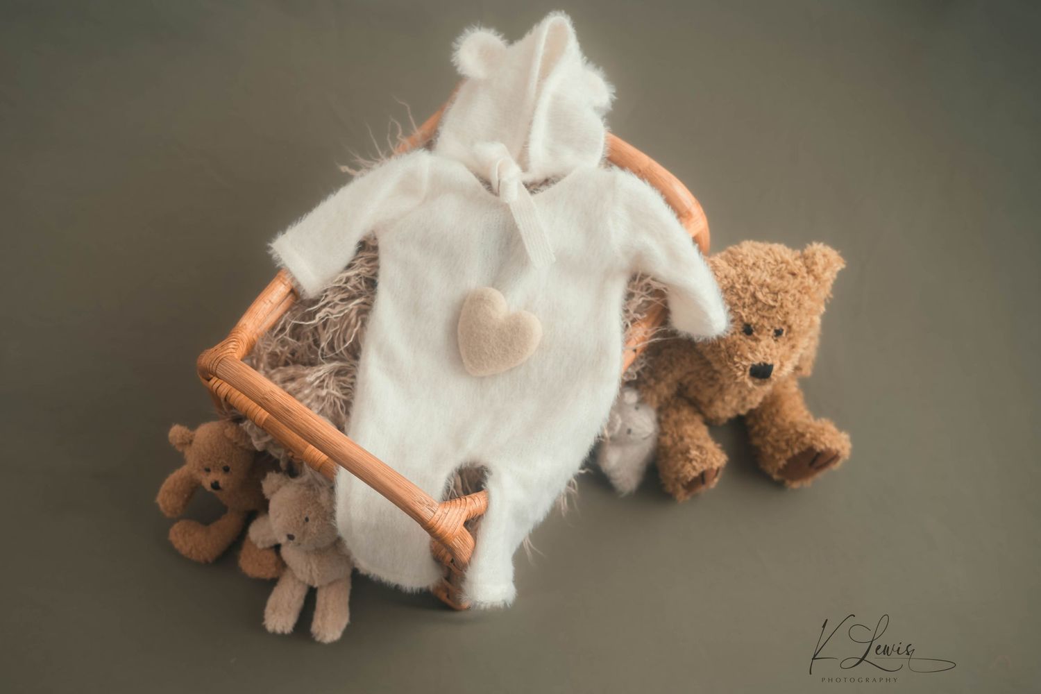 White bunny romper with heart detail in wicker basket surrounded by teddy bears, newborn photography prop.