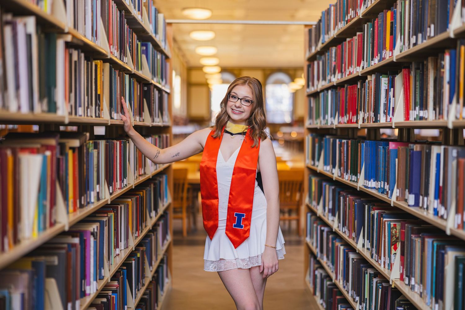 UIUC graduate leaning on bookshelves at the Main Library