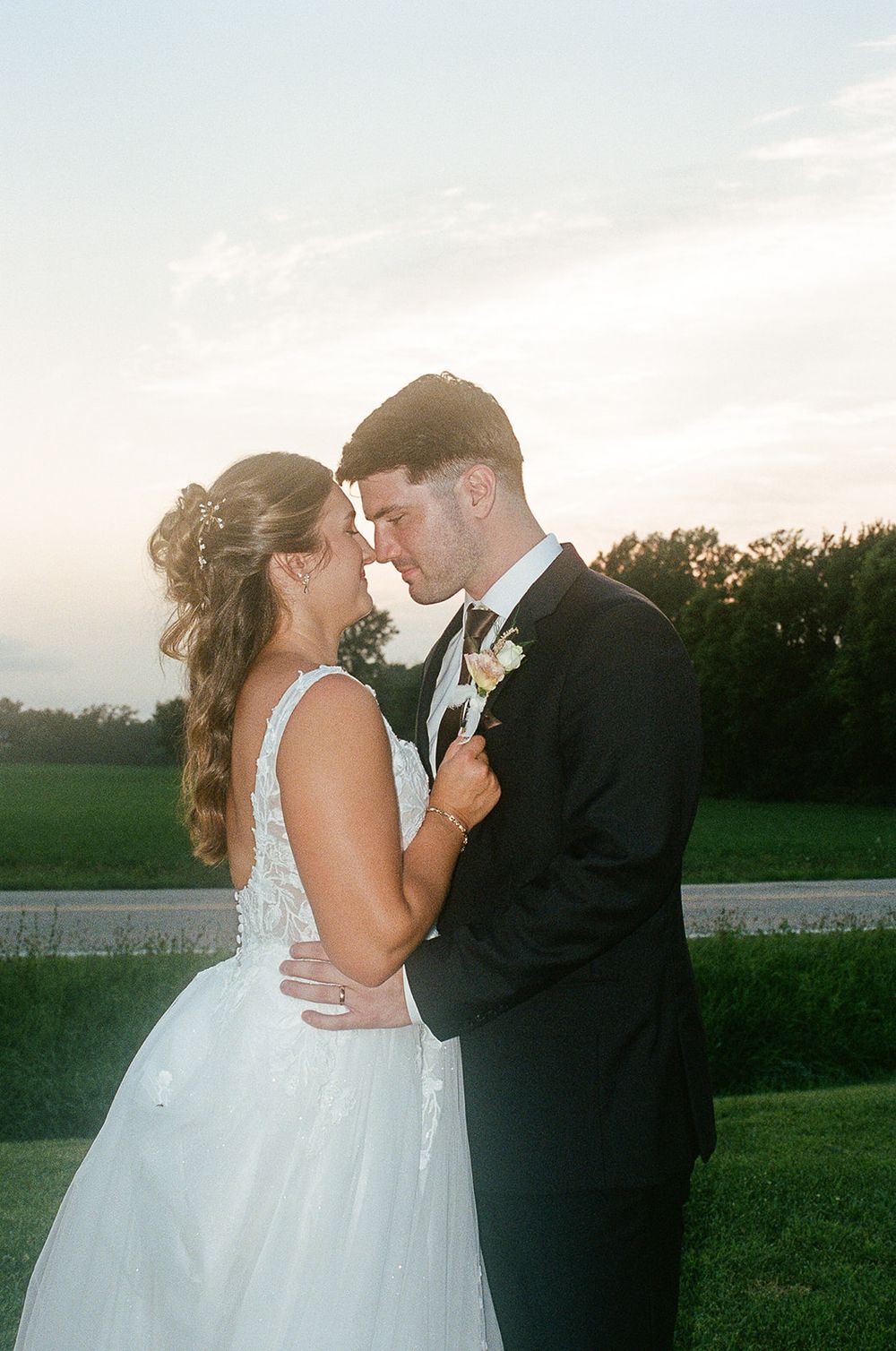 A bride and groom share a romantic forehead touch at sunset, surrounded by lush greenery on their wedding day.