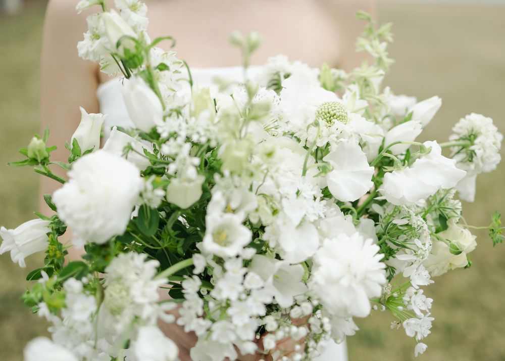 Close-up of lush white wedding bouquet with roses, ranunculus, and greenery.