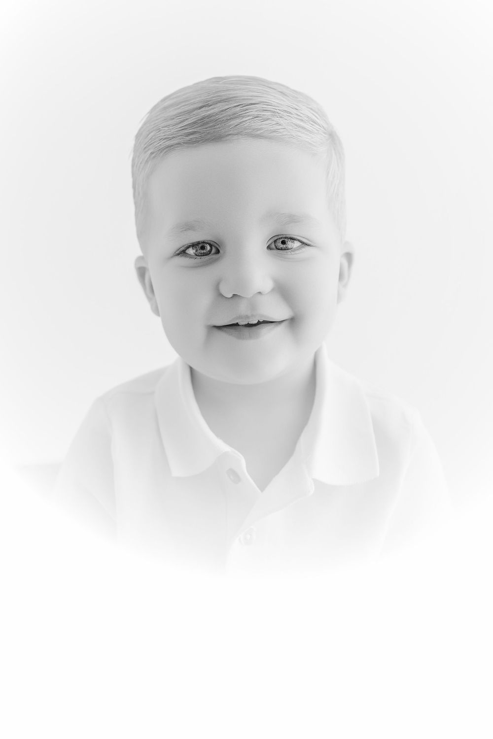 Black and white portrait of a smiling young boy with light hair wearing a white polo shirt.