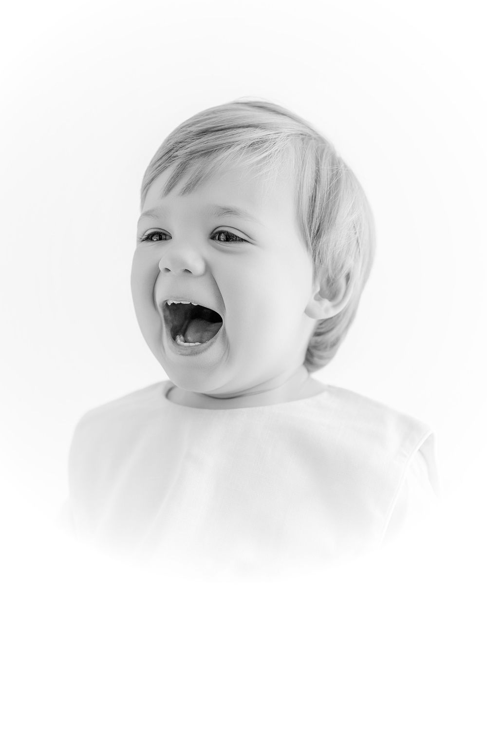 Black and white portrait of a laughing baby with mouth open wide, showing pure joy and happiness.