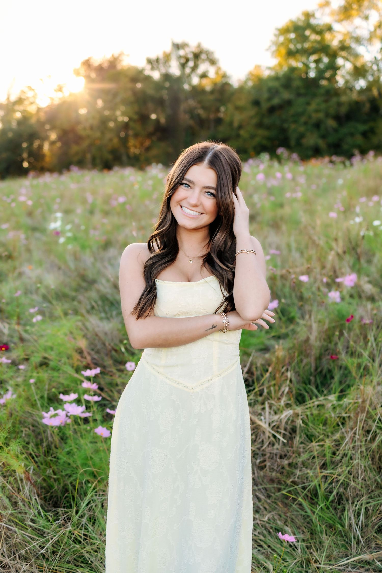 Senior girl in yellow dress smiling in a wildflower field at golden hour sunset.