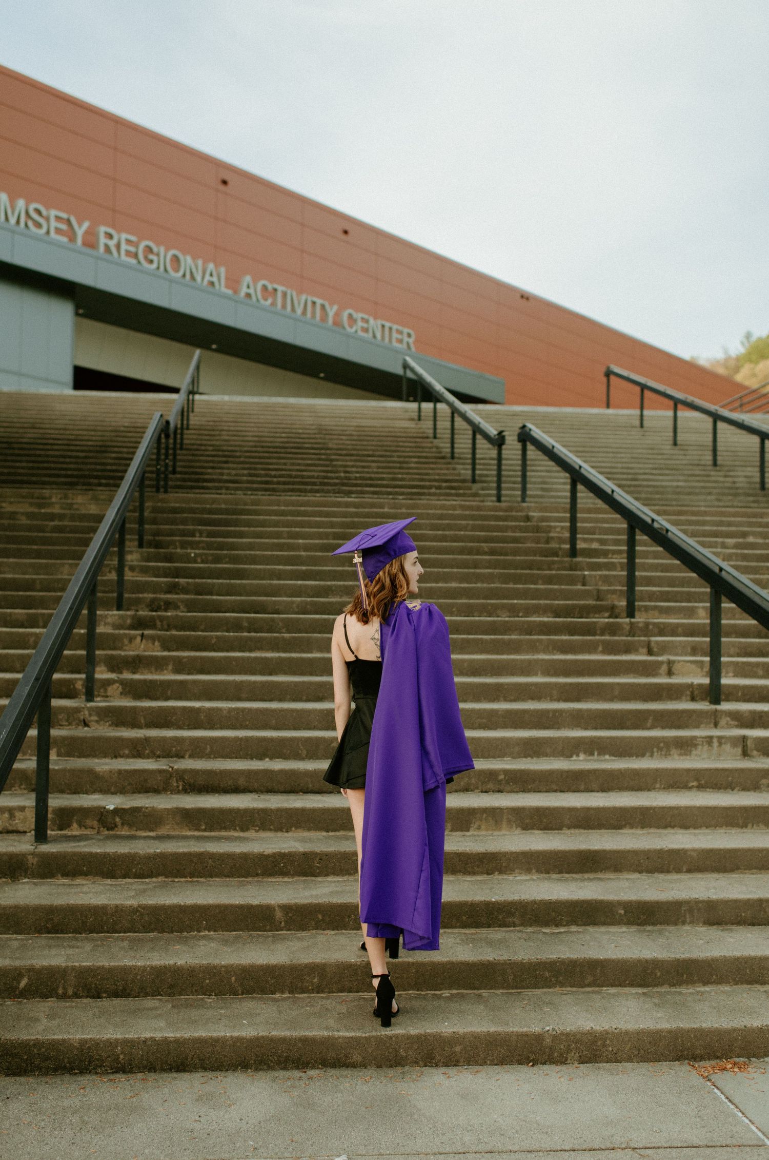 A purple graduation cap and gown hangs on concrete stairs outside a regional activity center building.