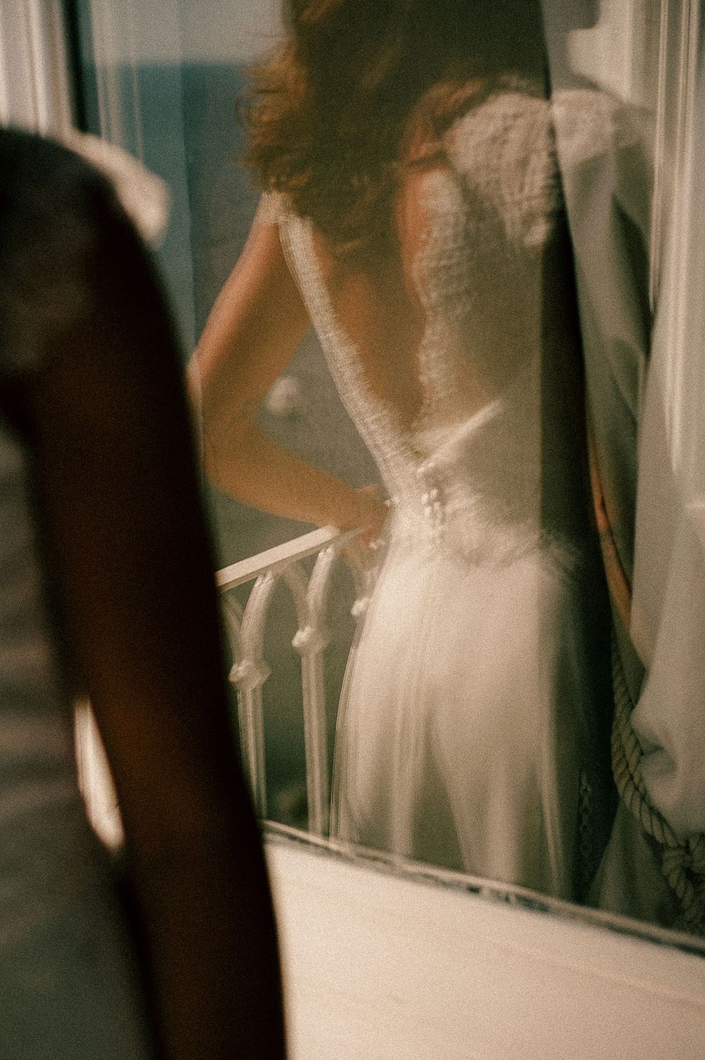 Bride in elegant lace wedding dress viewed from behind, reflected in a mirror with soft warm lighting.