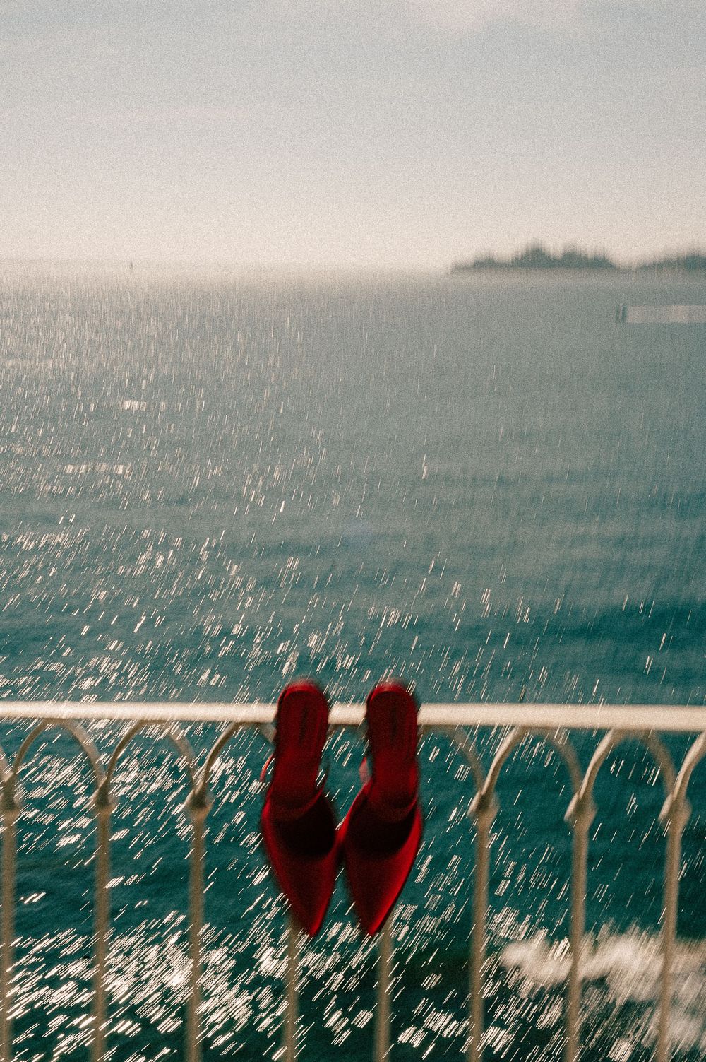 Red flip flops hanging on a white railing overlooking a sparkling turquoise ocean on a rainy day.
