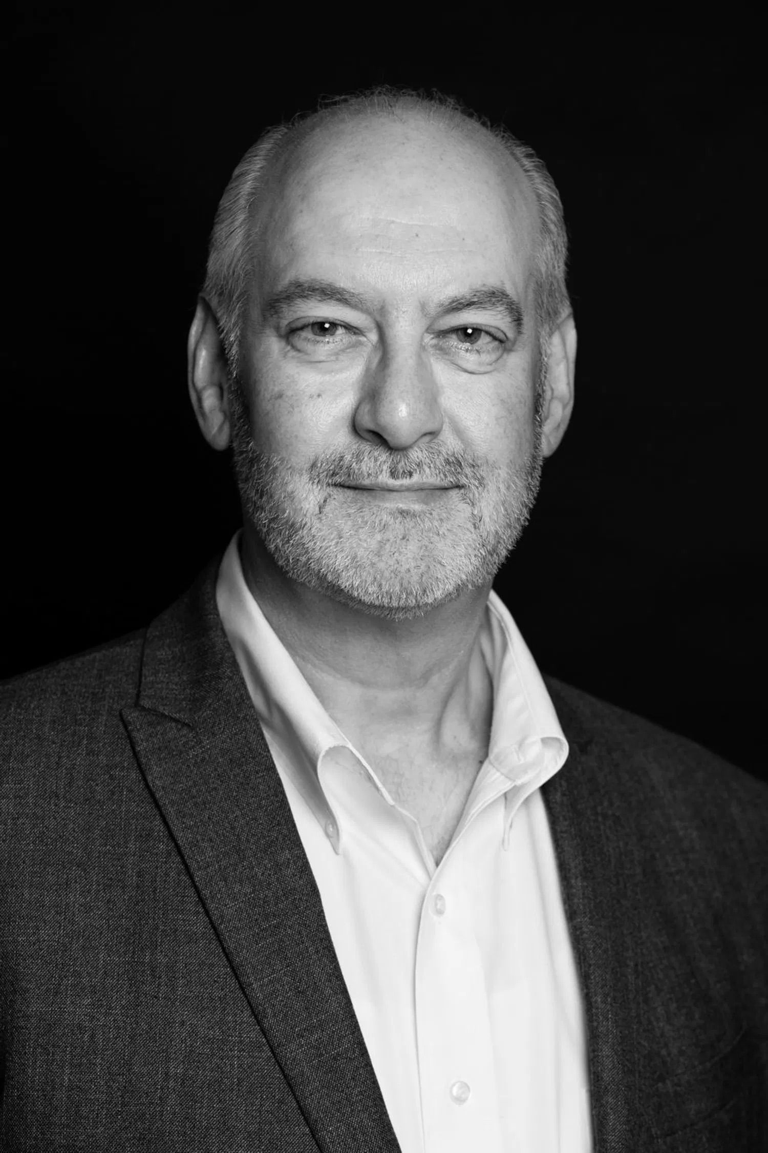 A middle-aged man with gray hair and a beard wearing a suit and smiling at the camera.