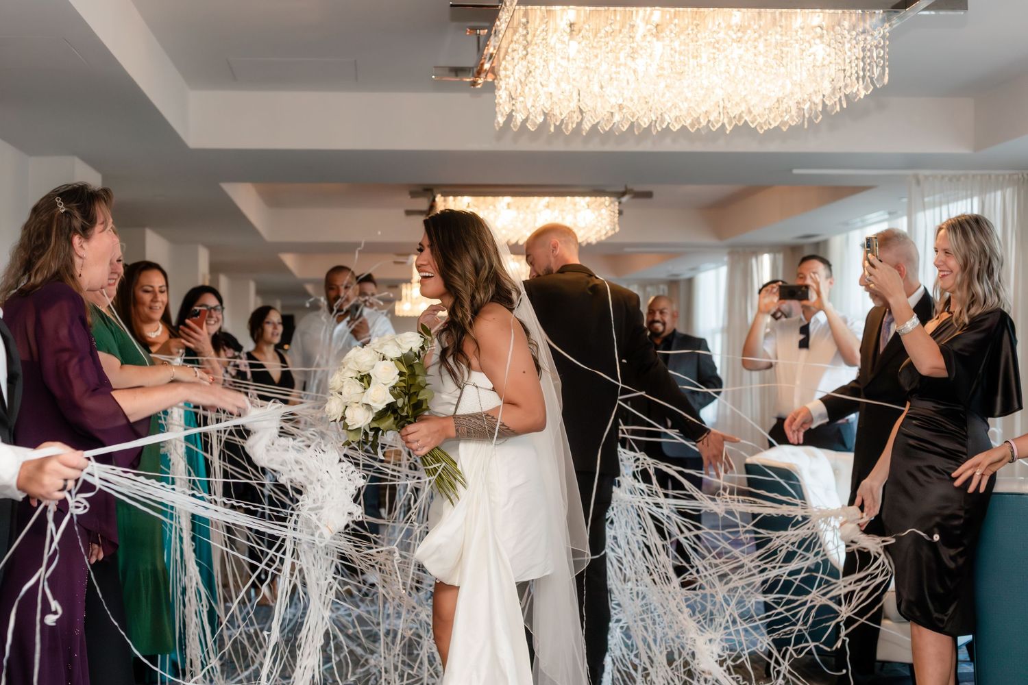 A sequence of wedding celebration photos showing guests playfully throwing streamers in an indoor venue with a crystal chandelier.