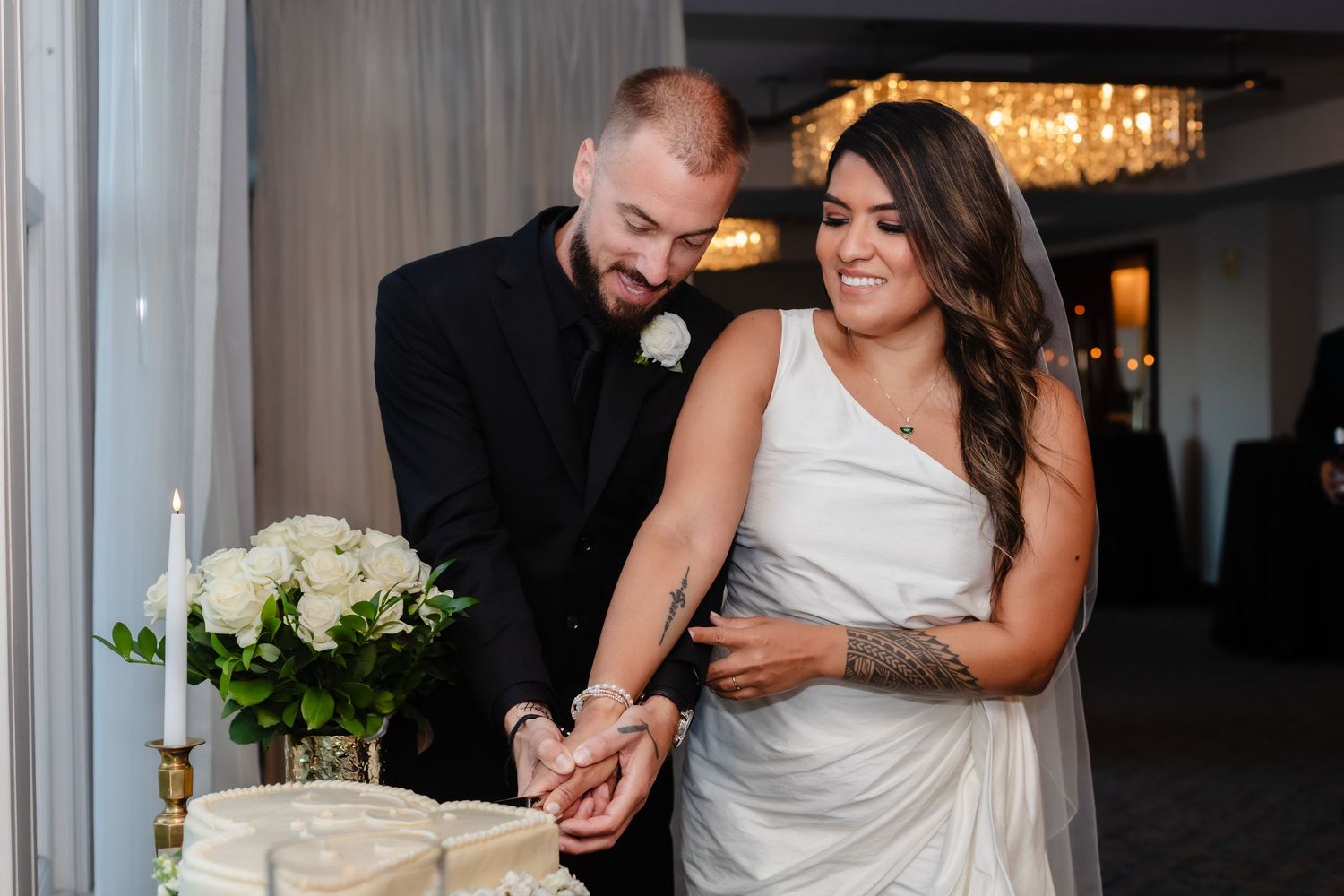 A couple shares a joyful moment while cutting their wedding cake together at an elegant indoor reception venue.