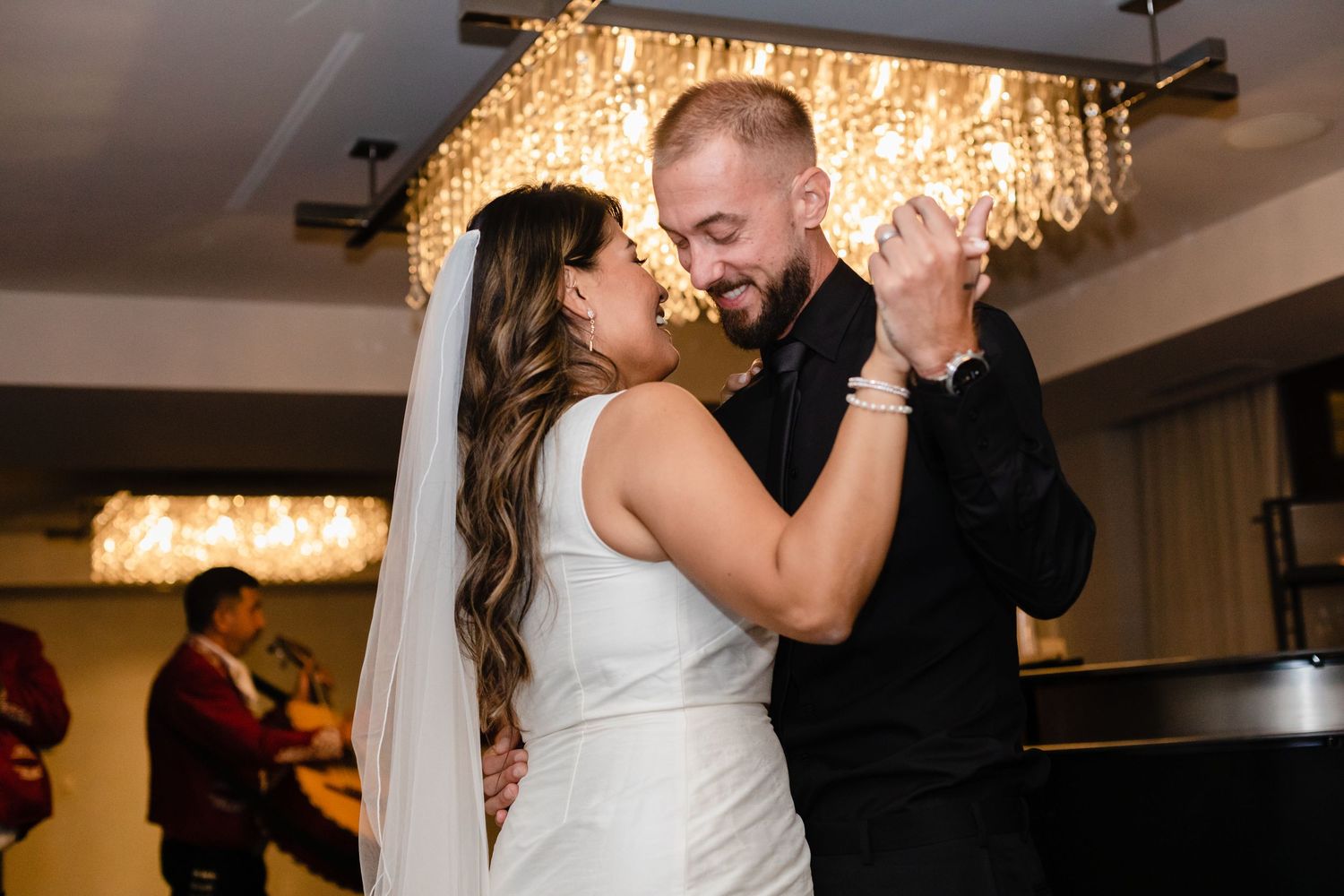 Couple shares romantic dance moments at wedding reception under crystal chandeliers and warm lighting.