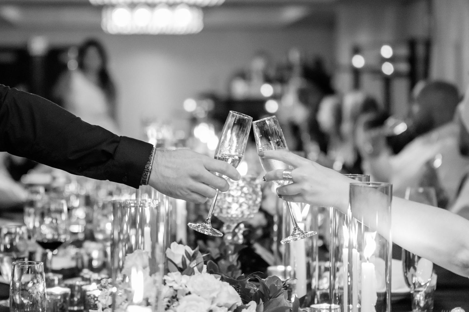 Hands raise wine glasses in a toast at an elegant dinner party with candlelit table settings.