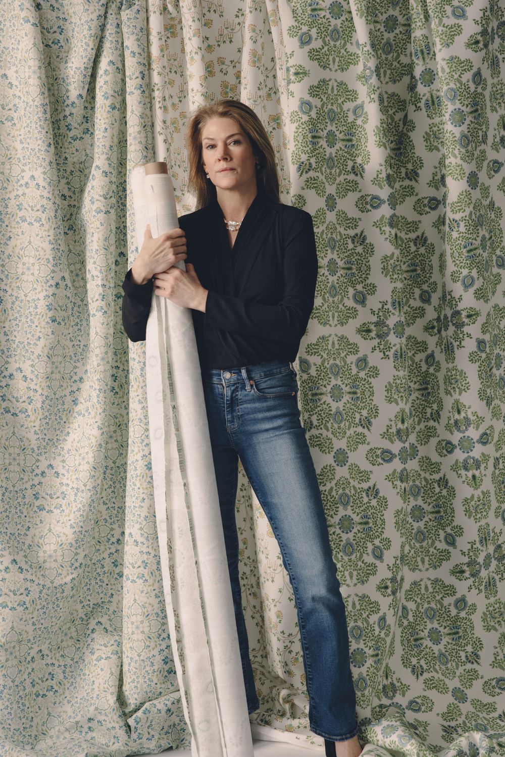 A series of four similar photos showing someone wearing jeans and a black top posing against a floral wallpaper background.