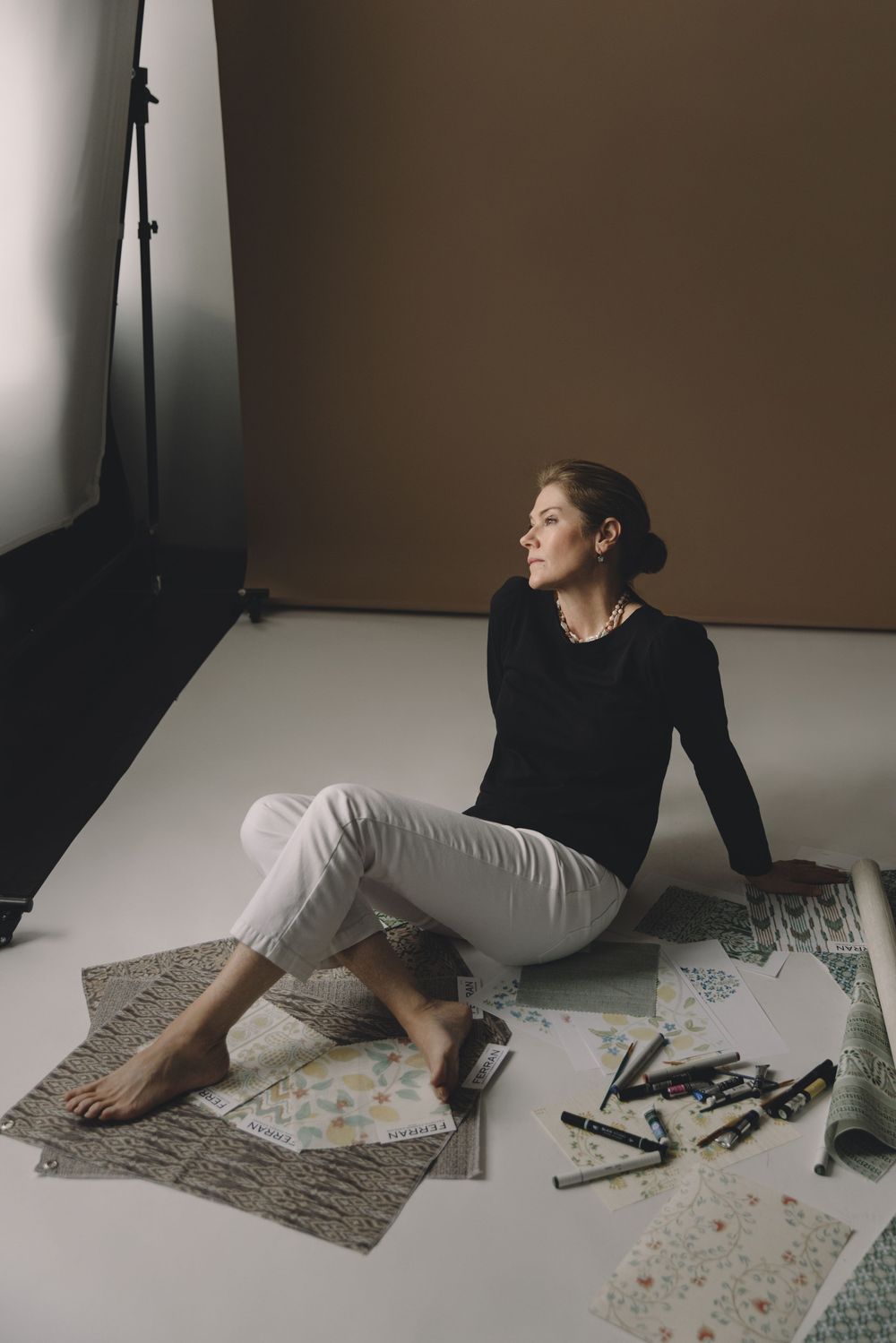 A person in dark clothing lies on a patterned rug in a minimalist room with dramatic lighting and shadows.
