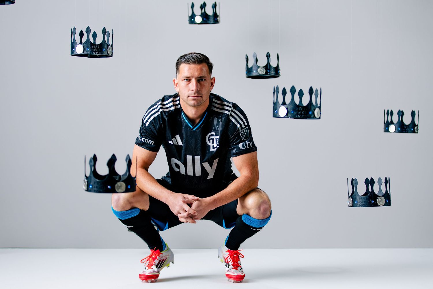 Charlotte FC player crouching in black Adidas jersey with ally sponsor surrounded by black crown decorations.