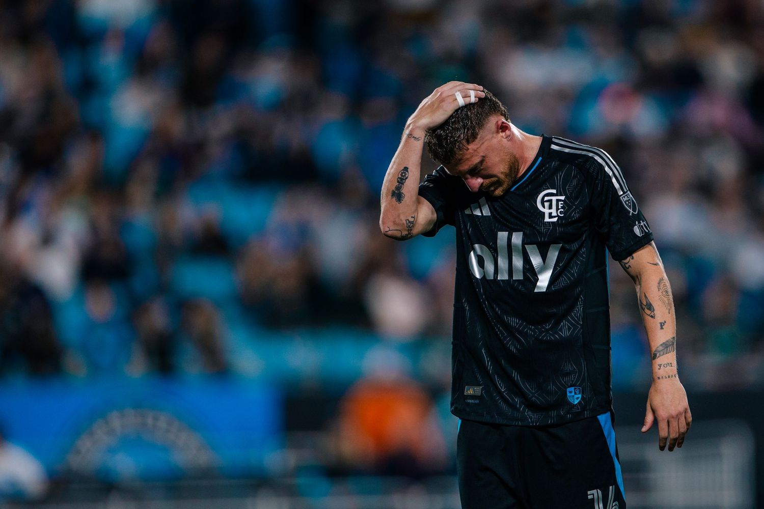 Charlotte FC player in black ally jersey holding head during match.