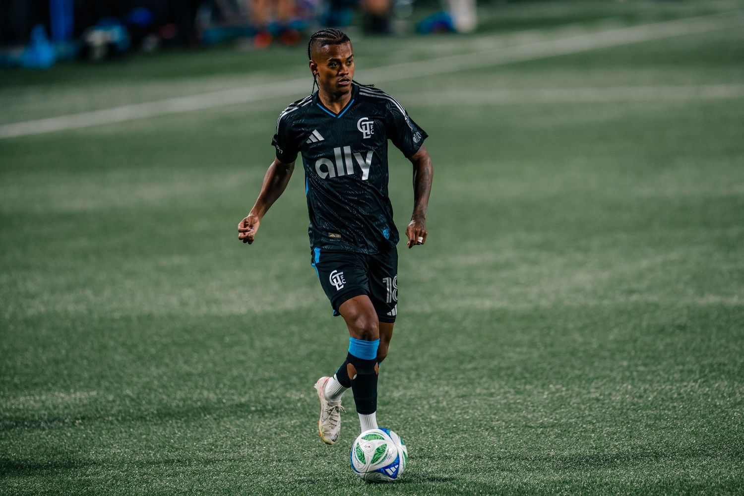Charlotte FC player in black Adidas ally jersey dribbling during evening match.