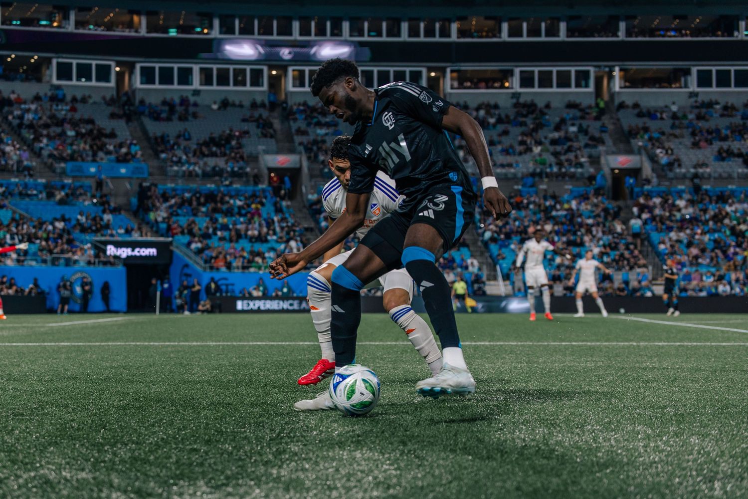 Charlotte FC player dribbling ball during nighttime MLS match in black jersey.