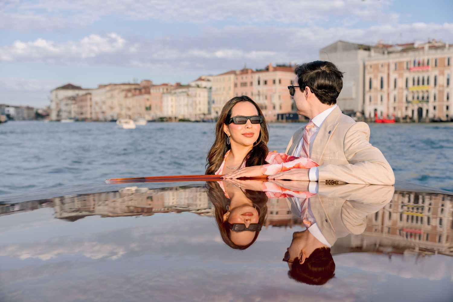 Two people enjoy a romantic moment by the canal in Venice, Italy with historic buildings reflected in the water.