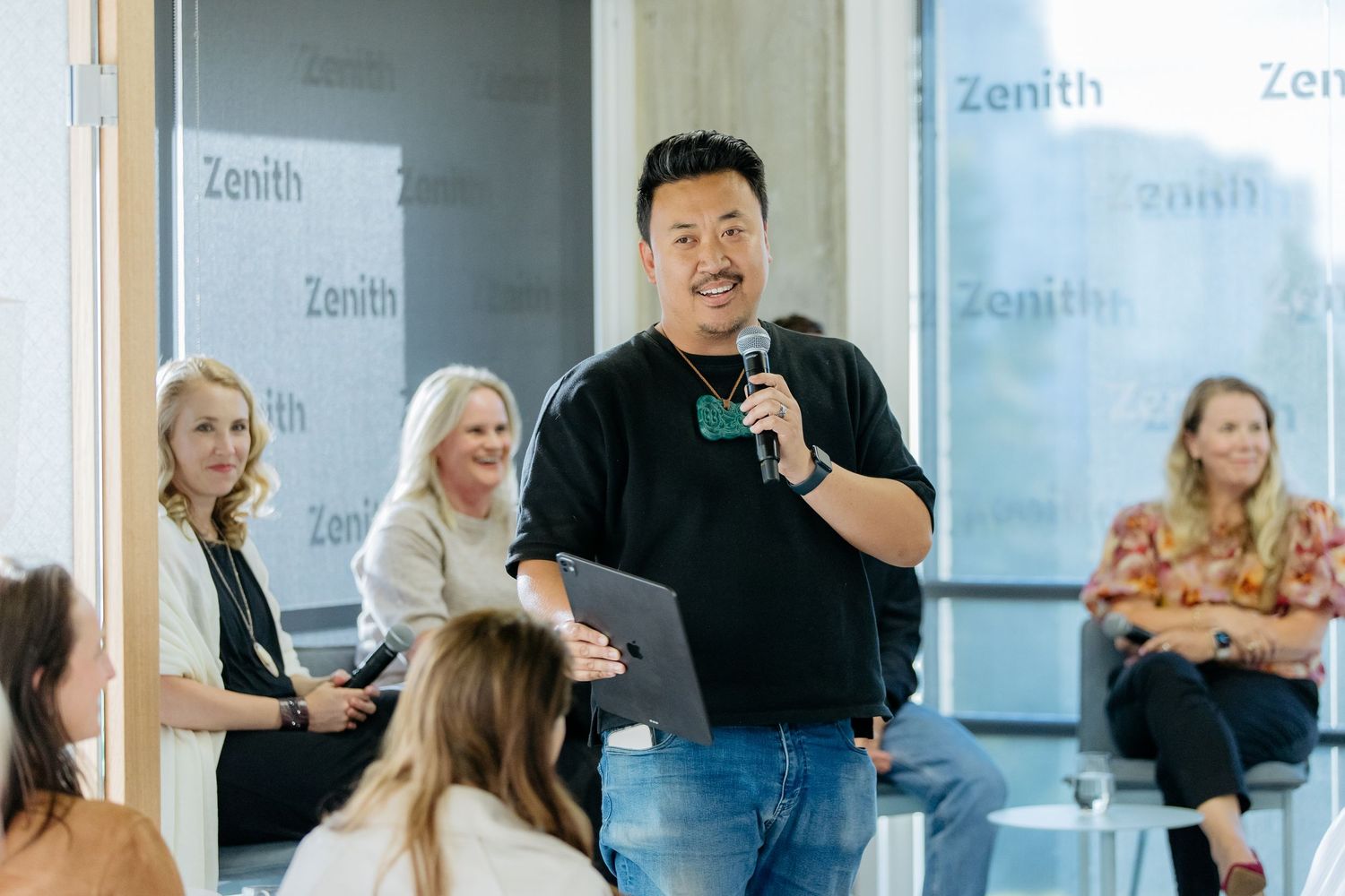 Corporate event photography in Auckland showing guest speaker talking to audience with a panel of experts in the background