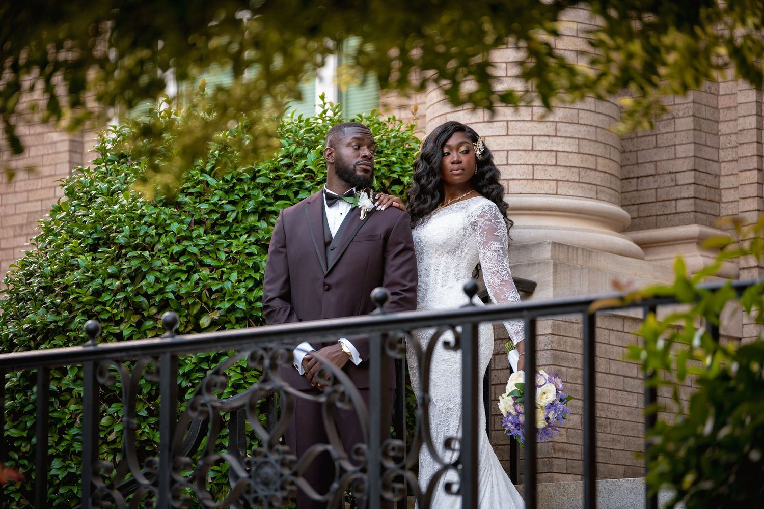 A couple in wedding attire shares a romantic moment on a brick staircase surrounded by lush greenery.
