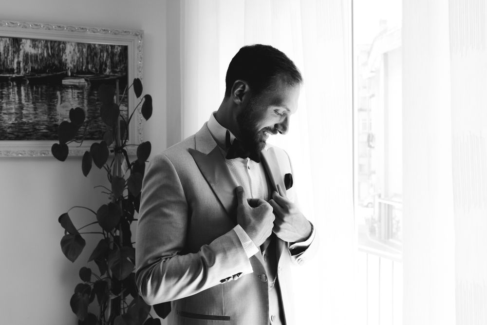 Portrait of the groom in an elegant suit near the window during the wedding preparations in Imperia.