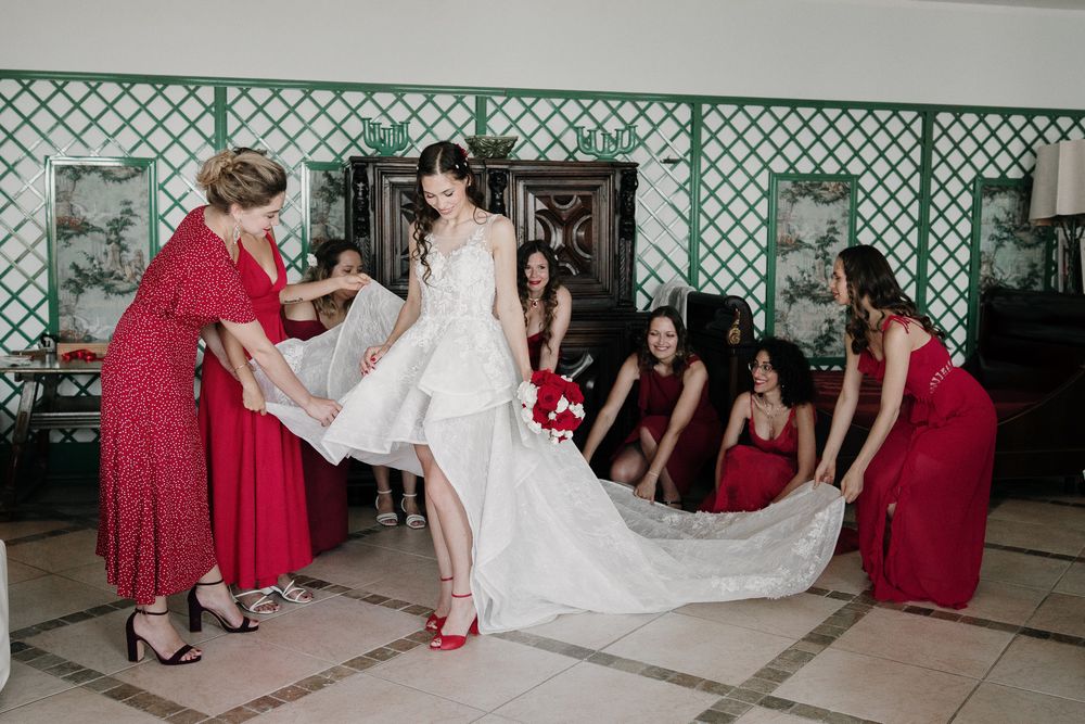 Bridesmaids in red dresses help the bride with a red and white bouquet before the ceremony