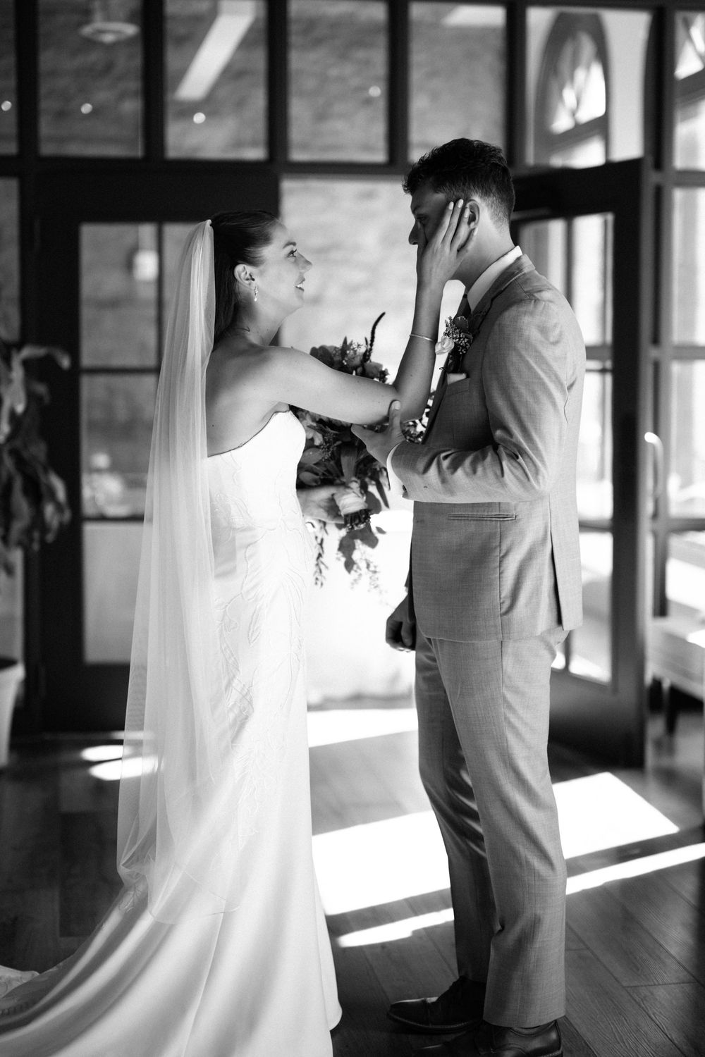 A black and white wedding photo series showing intimate moments between a bride and groom in a sunlit hallway.
