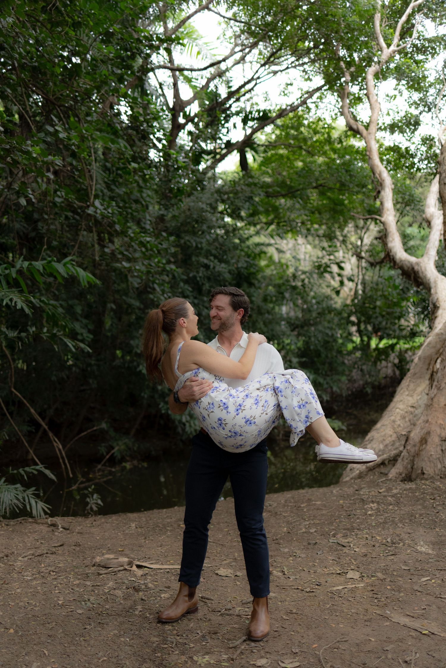 A romantic moment captured in a lush garden setting as a couple embraces in a playful lift pose.