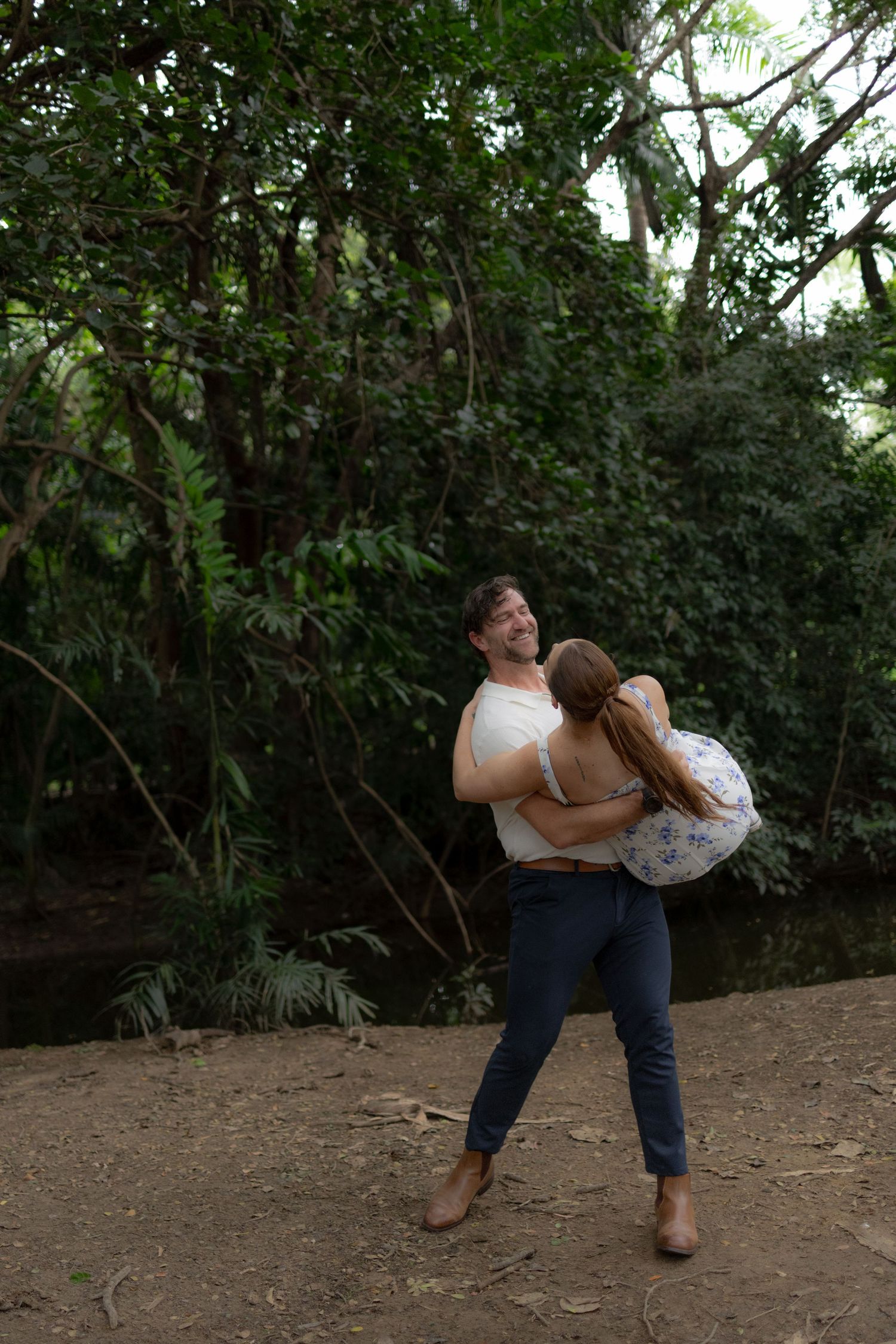 A couple shares a romantic dip pose in a wooded outdoor setting.