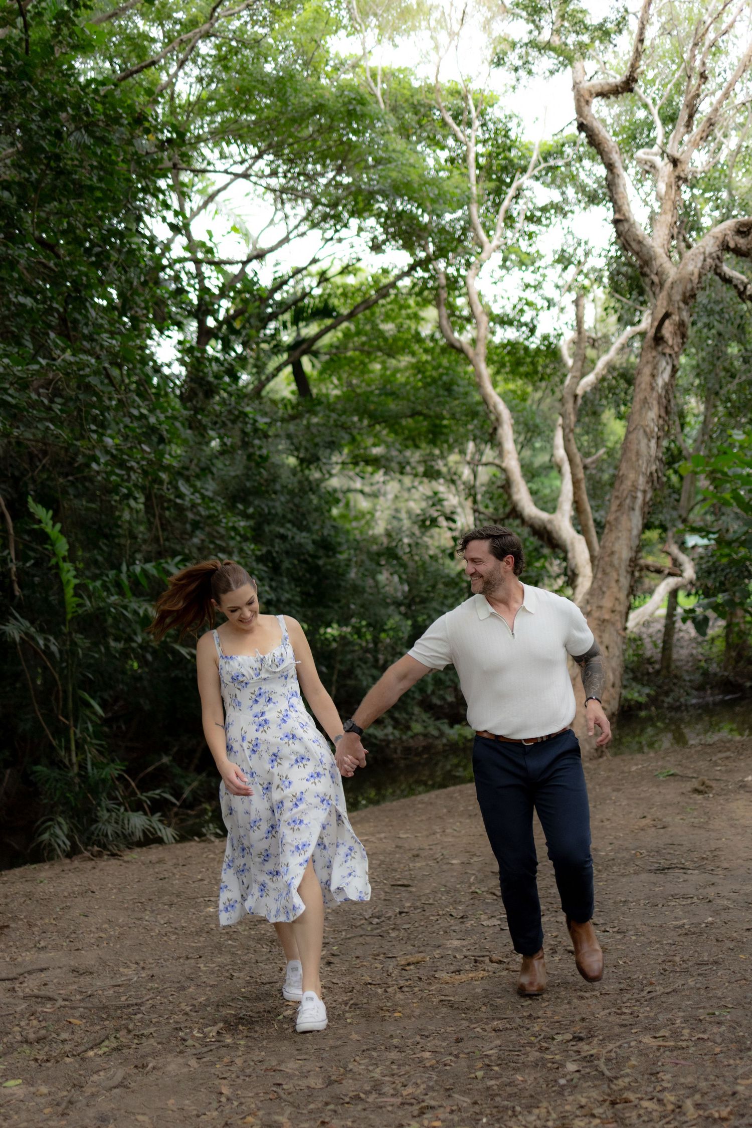 A couple playfully walks together through a wooded area on a sunny afternoon.