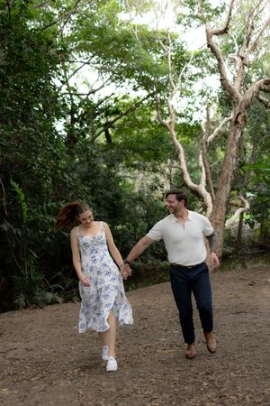 Couple walking and playing together on a dirt path surrounded by lush green trees in a natural setting.