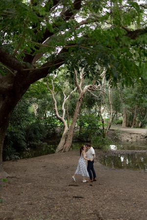 A couple walks hand in hand through a scenic grove of twisted old trees in a natural setting.