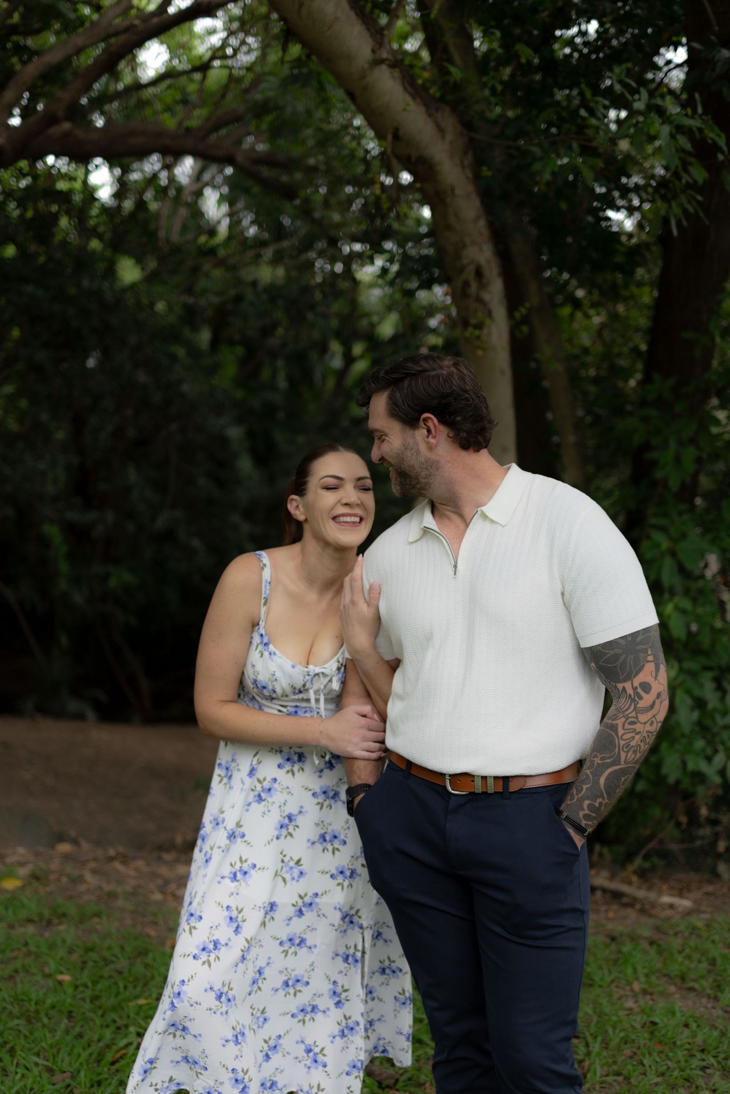 A couple shares laughter while standing together in a lush garden setting.