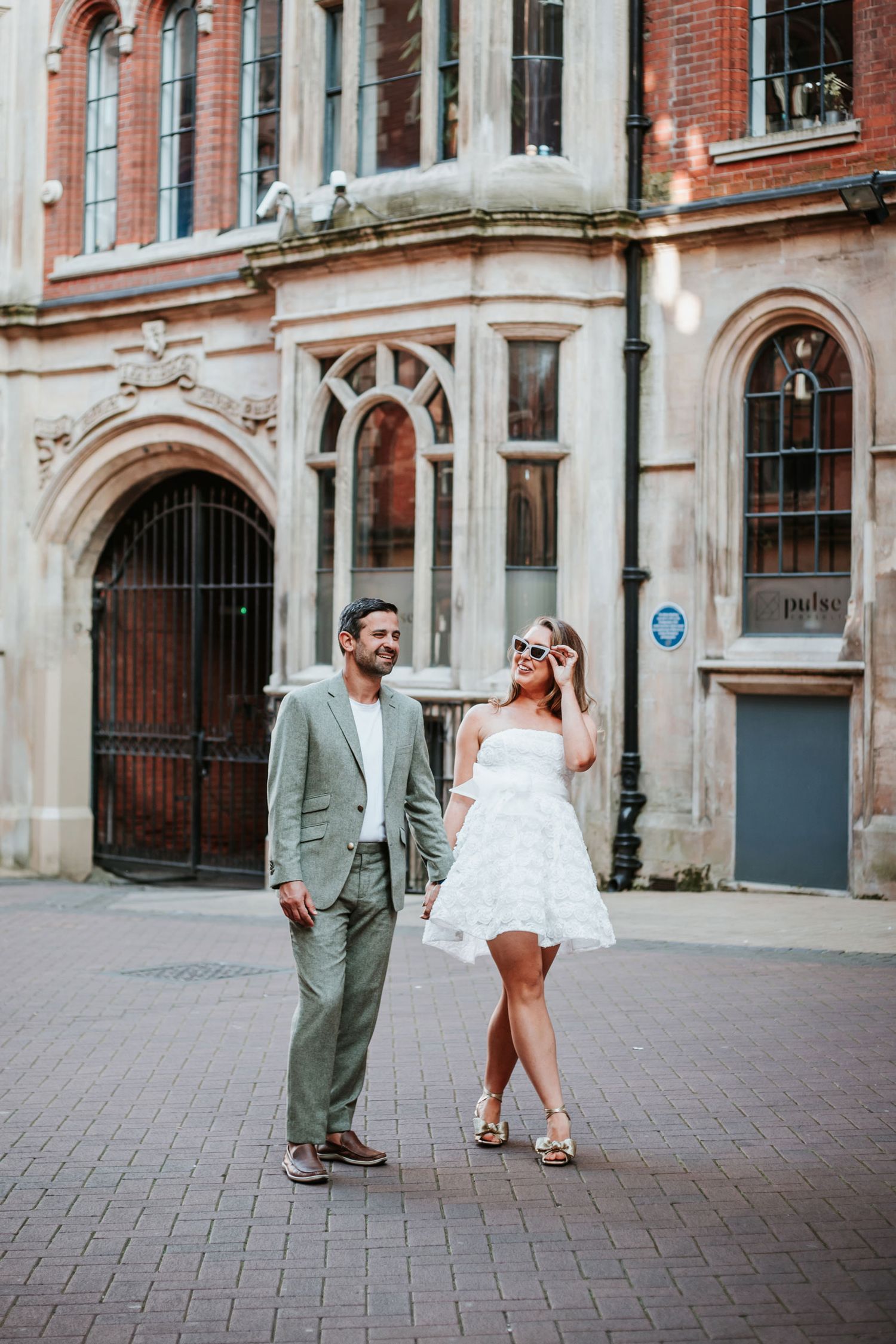 A couple dances playfully together on a cobblestone street in front of a historic brick building.