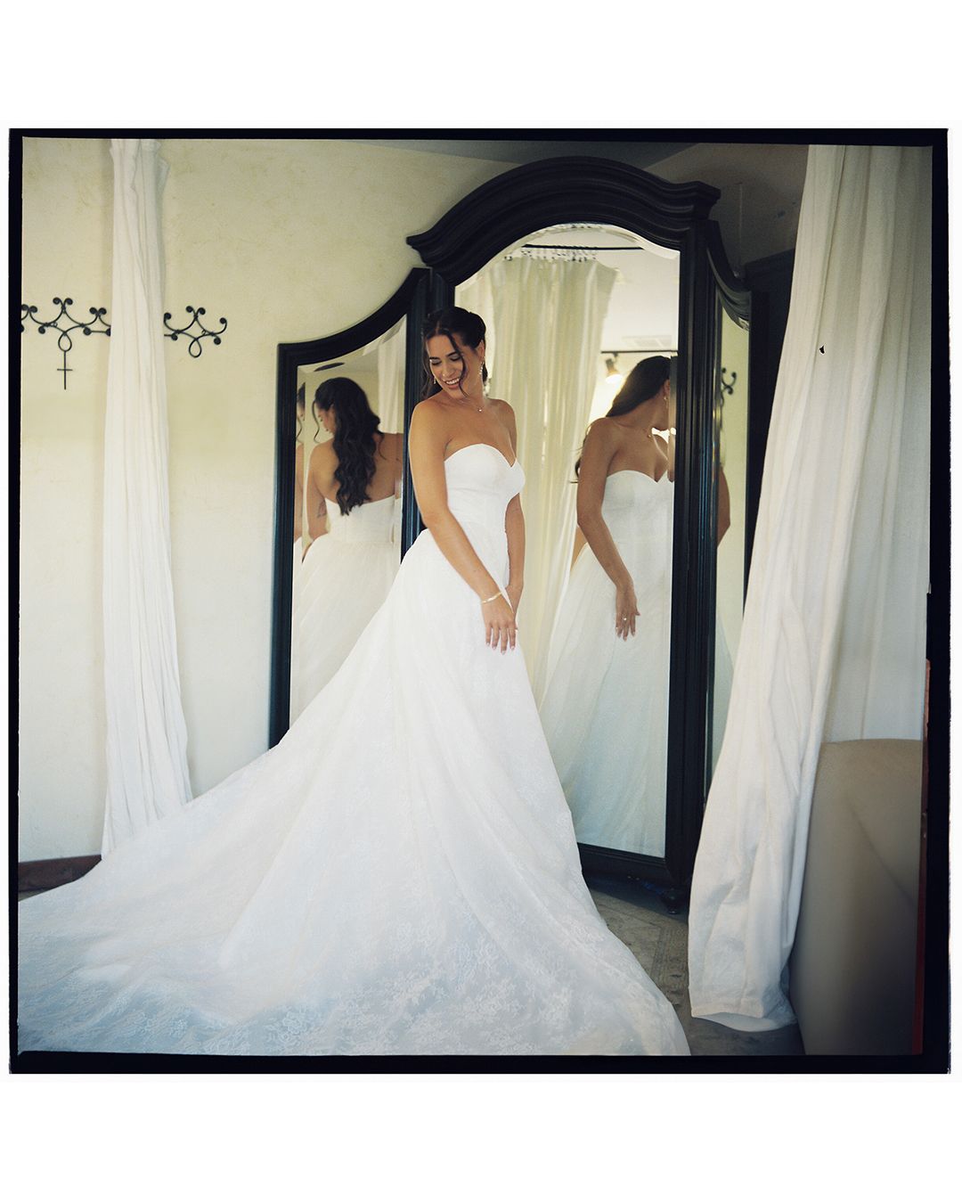A bride in a flowing white ball gown poses elegantly in front of a mirror, creating a stunning bridal reflection.