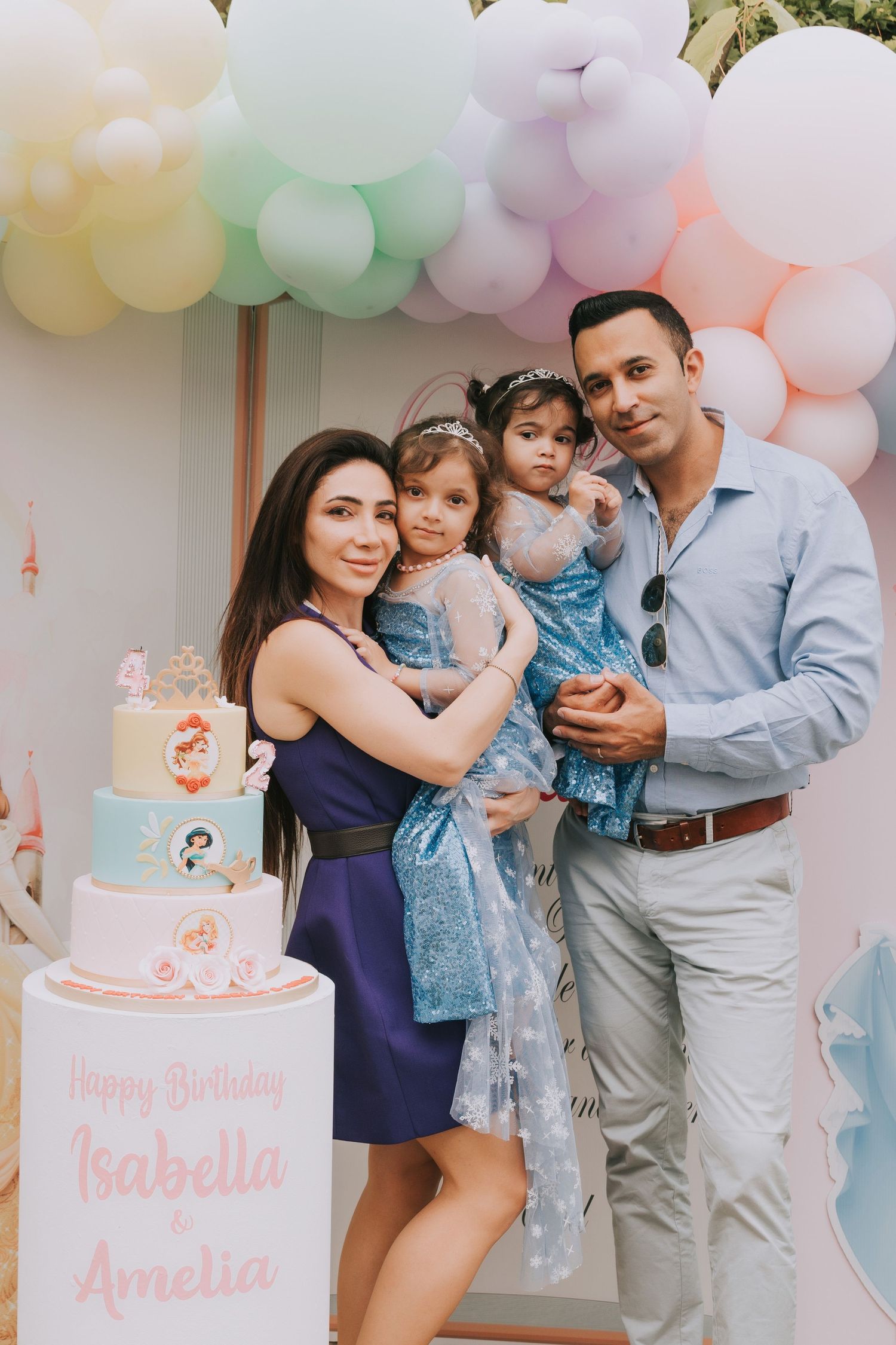 A family celebrates a birthday party with pink and white balloon decorations and a pink birthday cake.